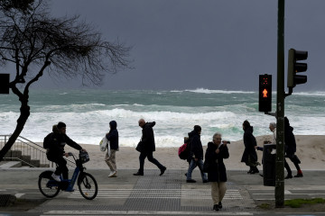 Archivo - Varias personas caminan delante de las olas durante el frente meteorológico, a 23 de febrero de 2024, en A Coruña