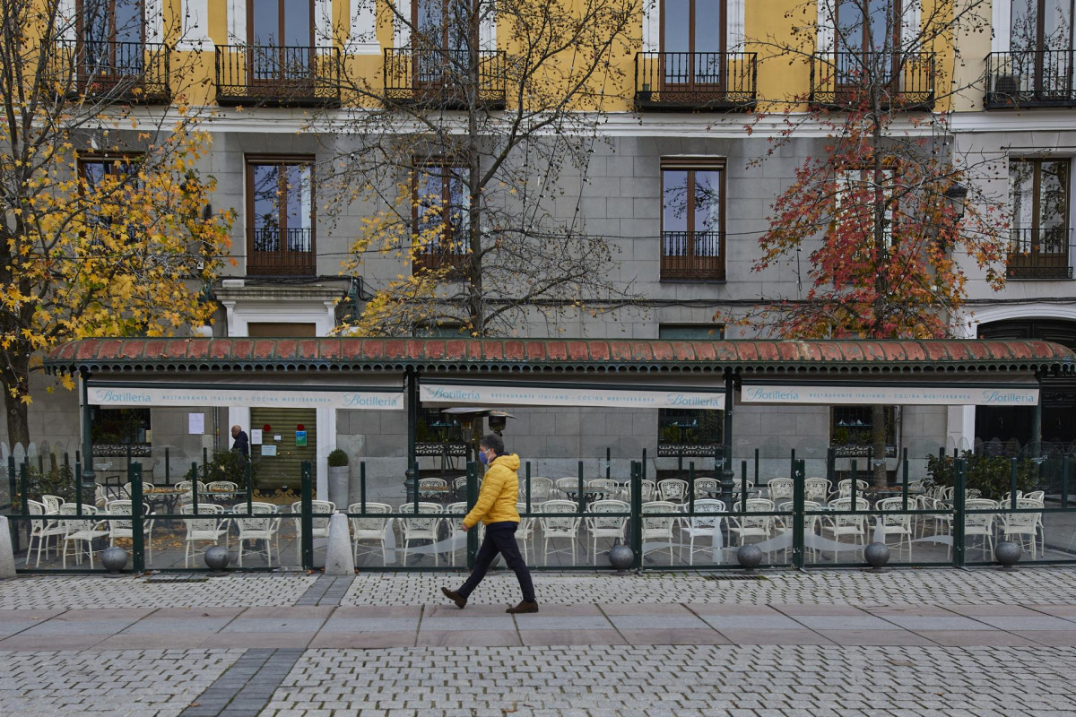 Una persona pasea al lado de una mampara instalada en un restaurante de la Plaza de Oriente, en Madrid (España), a 12 de noviembre de 2020. La Comisión de Terrazas de la capital acordó ayer una resolución por la que se permite, de forma temporal, la insta