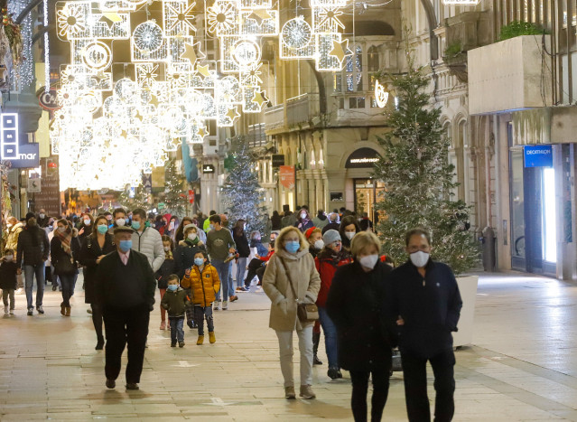 Transeúntes pasean bajo las luces navideñas, llevando mascarilla, en Vigo, Galicia (España), a 25 de diciembre de 2020. Vigo está cerrada perimetralmente, pero abierta entre el 23 y 25 de diciembre para permitir encuentros familiares.