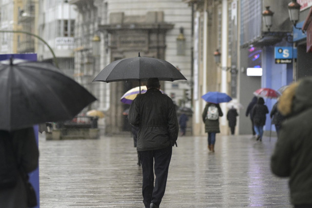 Transeúntes caminan protegidos por una vía de A Coruña.