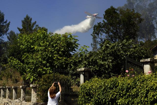 La propietaria de una finca afectada por un incendio forestal fotografía con su teléfono móvil cómo un hidroavión arroja agua sobre el fuego, a 28 de julio de 2021, en la parroquia de Santa Mariña do Monte, Ourense