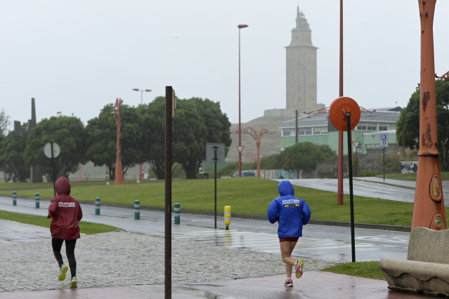 Archivo - Dos personas corren con chubasqueros cerca de la torre de Hércules, a 19 de junio de 2022, en A Coruña, Galicia, (España). La inestabilidad se mantendrá en Galicia al menos hasta la mitad de la semana que viene. A partir de mañana lunes 20 de ju