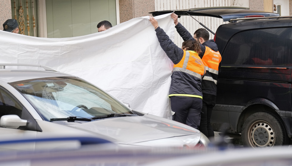 Dos agentes de Protección Civil tapan con una lona la zona donde se han encontrado los cuerpos de dos octogenarios en Sigüeiro.