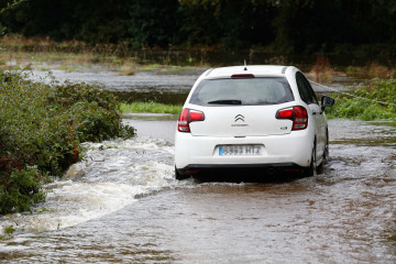 Un coche circula por un camino anegado por el desbordamiento del río Anllo, a 9 de octubre de 2024, en A Veiga, Abadín, Lugo, Galicia (España). La Agencia Estatal de Meteorología (AEMET) ha puesto