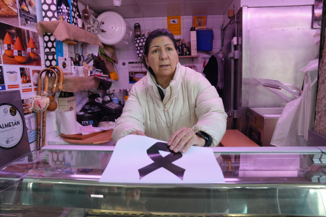 Una mujer coloca un crespón negro en una carnicería en la plaza de Abastos de Santiago, donde mataron al dueño de una carnicería