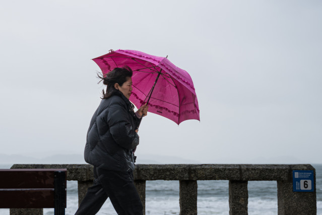 Una mujer se refugia de la lluvia con paraguas en el litoral gallego.